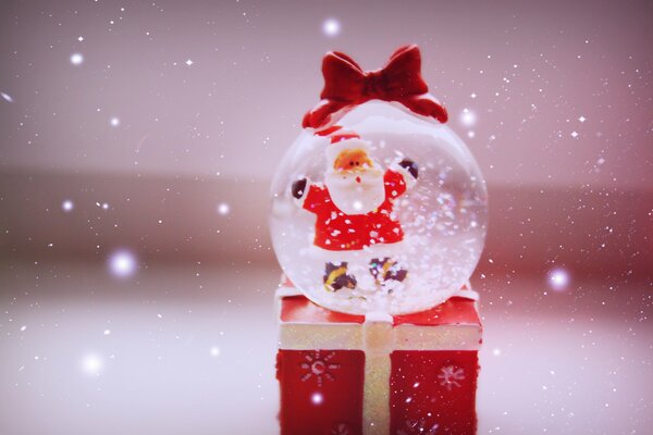 A funny Christmas ball with Santa Claus is lying on a red box