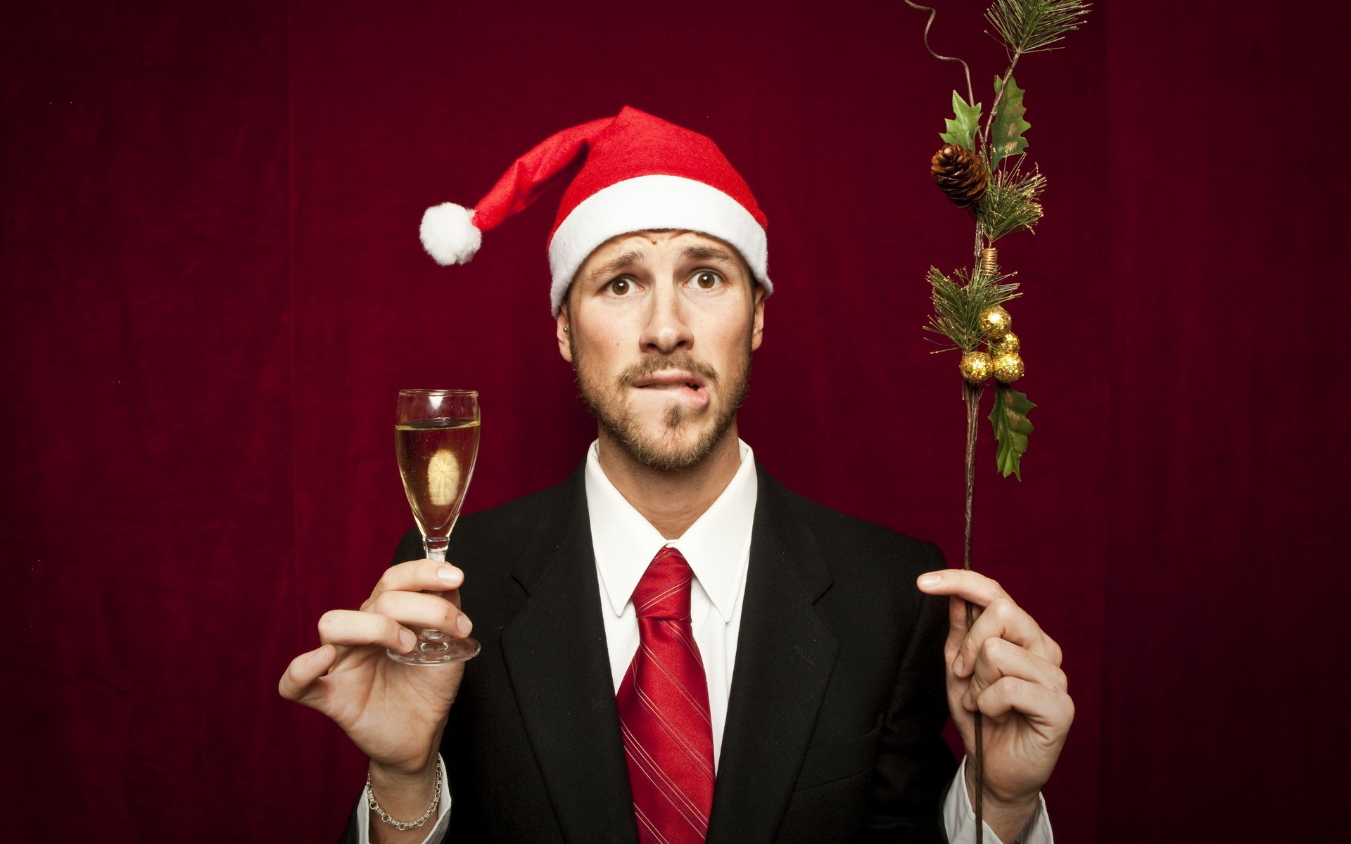 new year guy in a suit congratulates in the cap with a glass champagne fur-tree branch christmas background