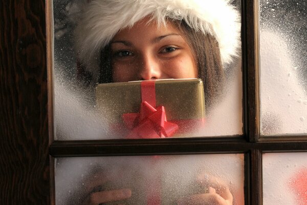 A girl in a hat and with a gift in her hands, looks out the window