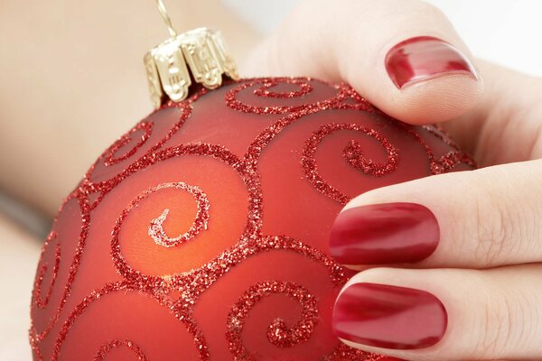 La mano con la manicura roja sostiene el juguete rojo del árbol de Navidad