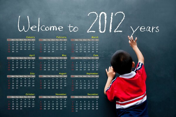 The boy writes with chalk on the blackboard