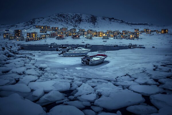 Pueblo nocturno en la costa. Barcos en témpanos de hielo agrietados