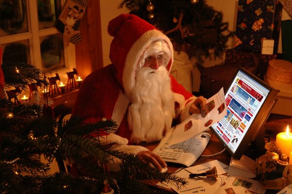 Der Weihnachtsmann hinter dem Laptop in einem gemütlichen Raum