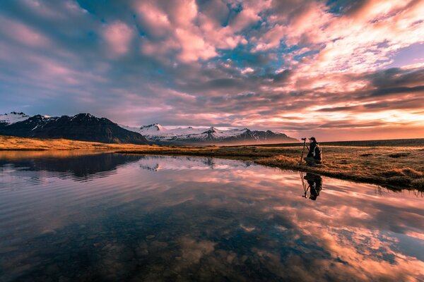 A photographer on the shore of a lake shoots a sunset in the mountains