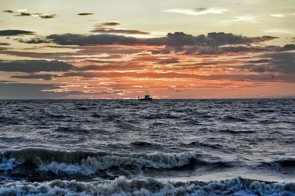 Un barco en medio de una puesta de sol en un mar furioso