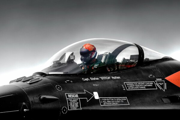 A helmeted pilot sits in the cockpit of a black plane