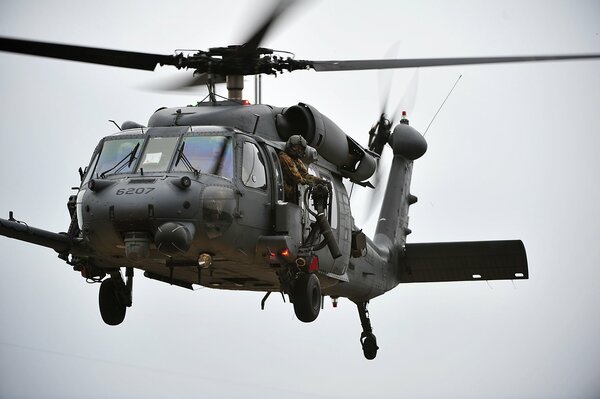 A soldier with a machine gun is flying in a military helicopter