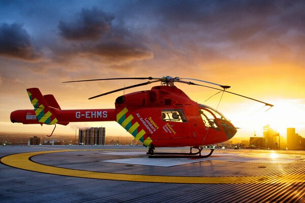 A red helicopter is standing on the landing at sunset