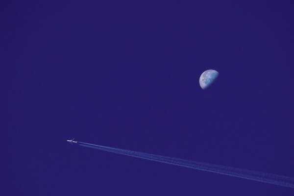 A passenger plane in the sky flying past the Moon leaves an inversion trail behind it