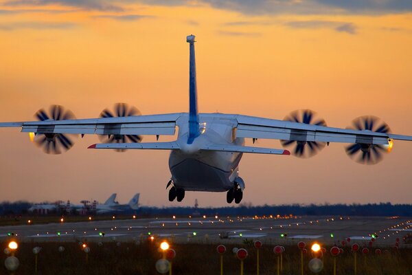 Aterrizaje del avión al atardecer. Se encienden las luces de la pista