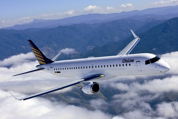 A white liner flies above the clouds against the background of mountains