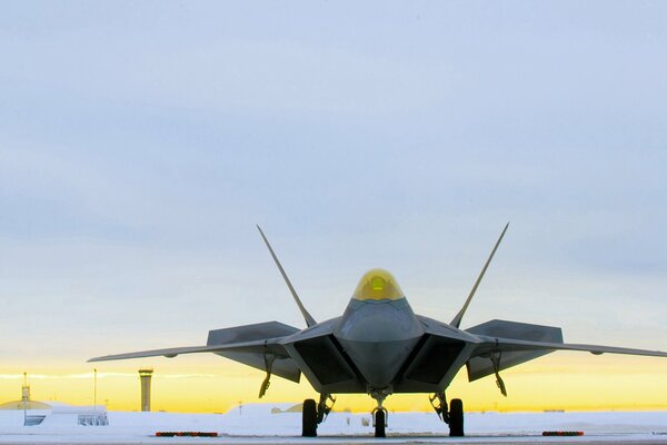 A raptor fighter stands at the airfield against the background of sunset