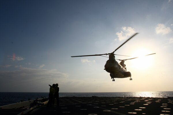 In the night sky over the ocean, a helicopter lands on the platform of an aircraft carrier