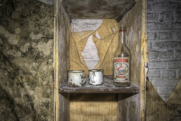 A bottle of vodka and two old mugs on the shelf