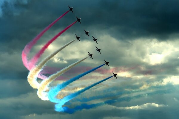 Several jet fighters, against the background of clouds, lead colorful plumes