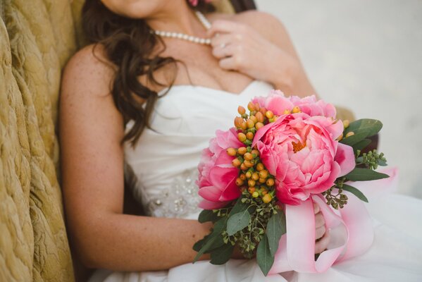 The bride holds a bouquet of peonies in her hands