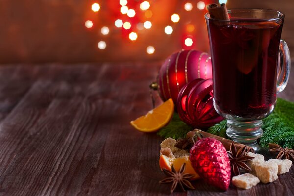 Ein Becher mit Glühwein auf einem Tisch mit Gewürzen und Weihnachtsspielzeug