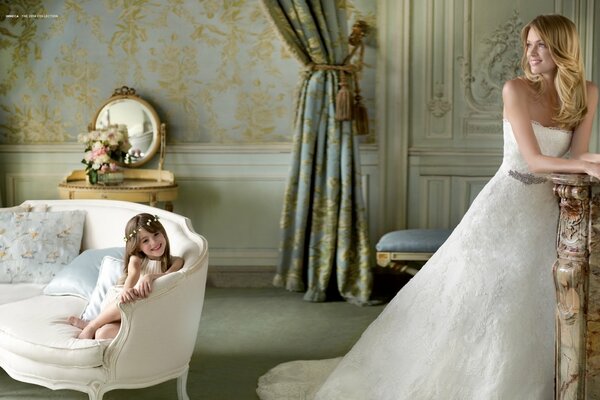 Feliz madre e hija en una sesión de fotos de bodas con vestidos blancos entre la decoración aristocrática de la habitación