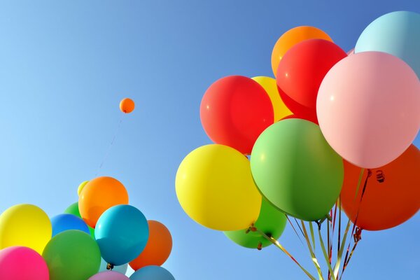 Two bundles of multicolored festive balloons on a blue sky background and one balloon in the distance