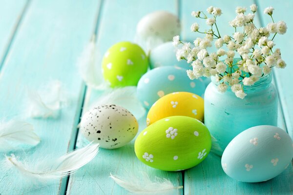 Oeufs de Pâques sur une table en bois bleu, vase bleu avec des fleurs et des plumes