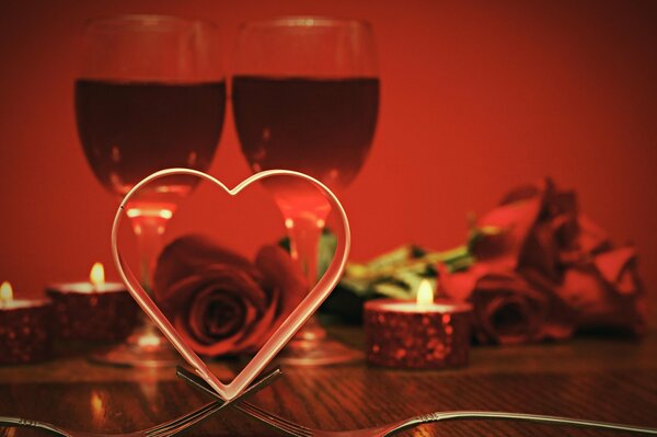 A ribbon folded in the shape of a heart against the background of two glasses, burning candles and roses