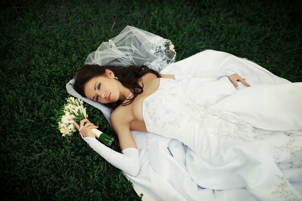 The bride in a wedding dress is lying on the grass