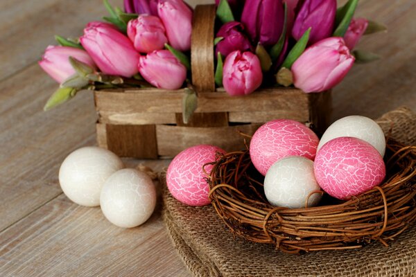 Ein Osterkorb mit Eiern und ein Korb mit Tulpen