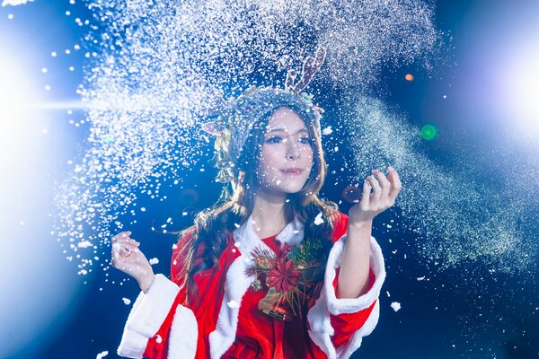 Mujer asiática con cuernos en traje de papá Noel arroja polvo brillante