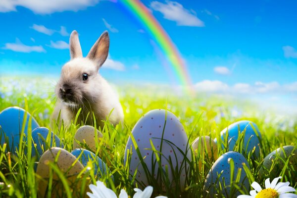 An Easter bunny is sitting in the grass against the background of beautiful eggs and flowers