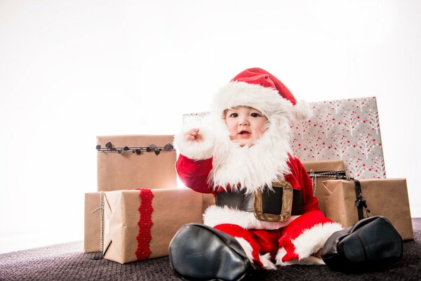 Un bambino in costume da Babbo Natale si siede sullo sfondo di Koro ok con regali e augura a tutti un Felice Anno Nuovo e Buon Natale