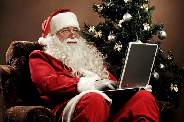 Santa Claus en una silla con una computadora portátil