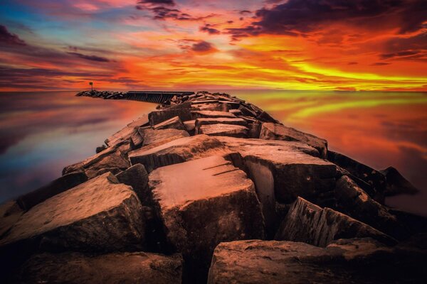 Amanecer rojo brillante es el mar entre el que se extiende un rompeolas