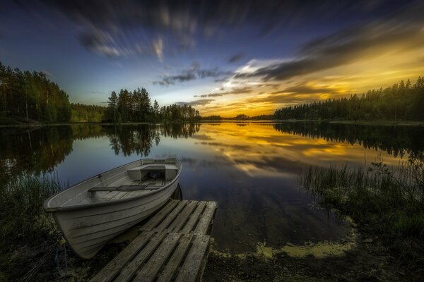 Mirror reflection of sunset colors on the lake. Boat at the bridge