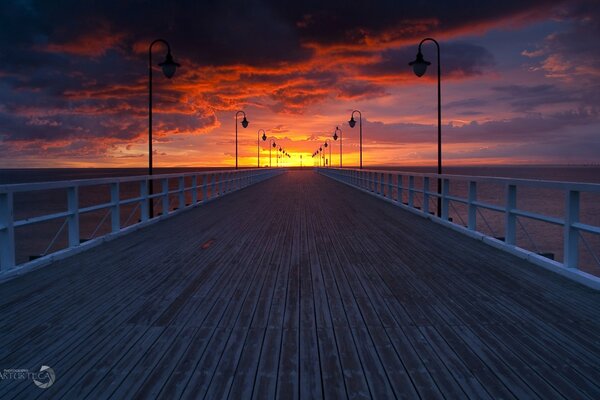 Ein langer Pier geht in die Ferne, wo man den Sonnenuntergang sehen kann