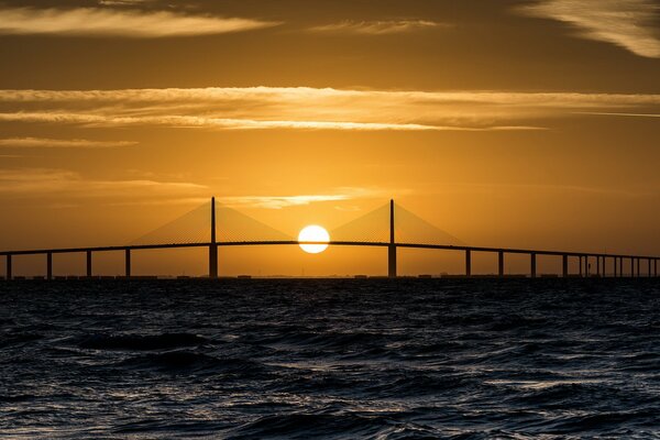 Orangefarbener Sonnenuntergang im Meer über der Brücke