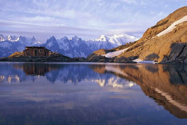 Cielo, cabaña y montañas en el reflejo del lago