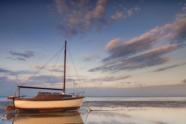 Sailboat on the beach by the sea against the sky with clouds