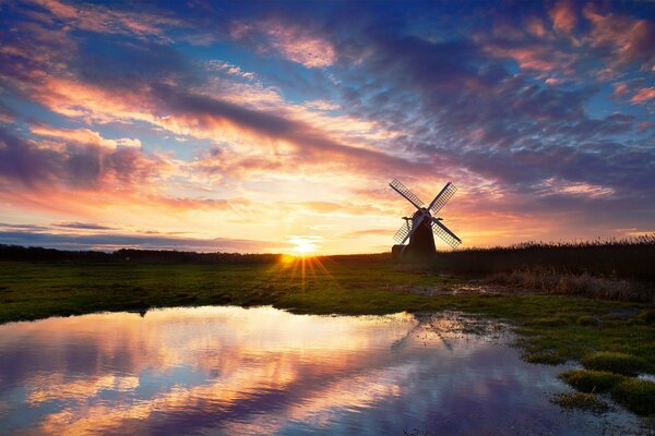 Die Mühle steht auf der Birke des Sees. Ein schöner Sonnenuntergang spiegelt sich im Wasser wider