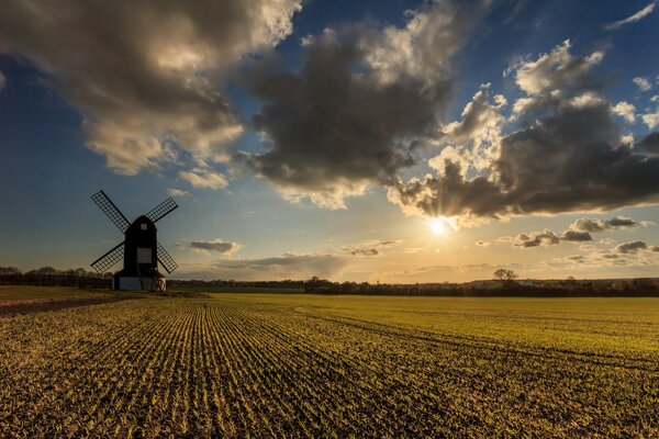 Il mulino in un campo infinito è illuminato dal sole che si fa strada tra le nuvole spesse