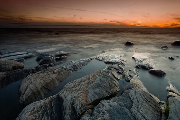 Spiaggia rocciosa contro il tramonto arancione