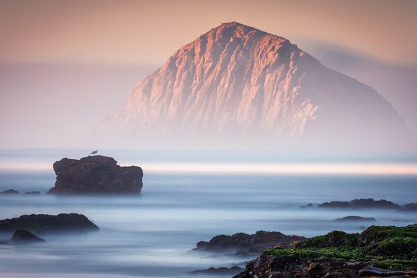 Rocas en la niebla contra el fondo de las montañas y el cielo rosa