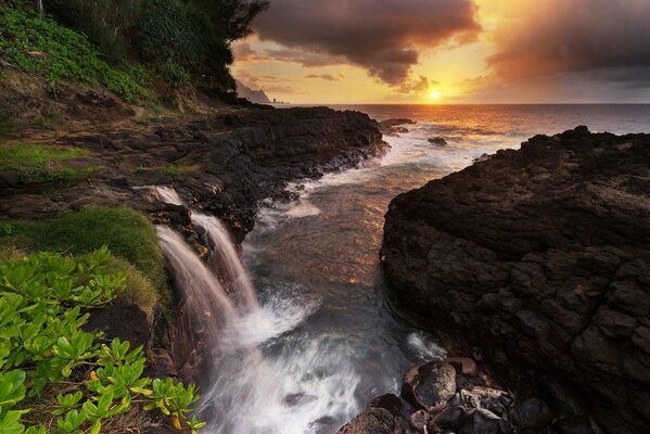 Waterfall on the background of the sea and rocks at sunset