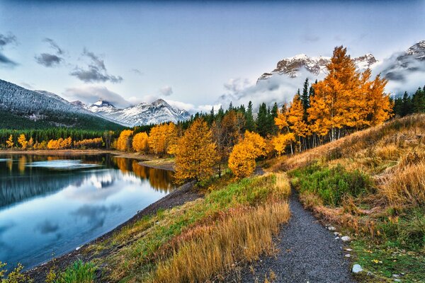 Autumn trees cover the hills. Snow-capped mountains can be seen in the distance. A river stretches along the autumn splendor