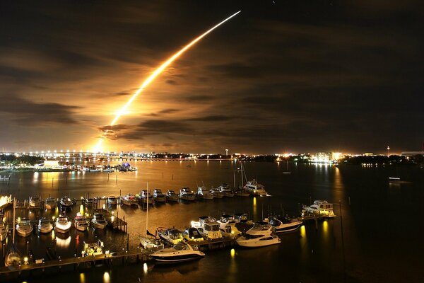 A trail of fire in the night sky over the marina with yachts