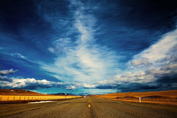 Un camino sin fin con un campo amarillo y un cielo nublado