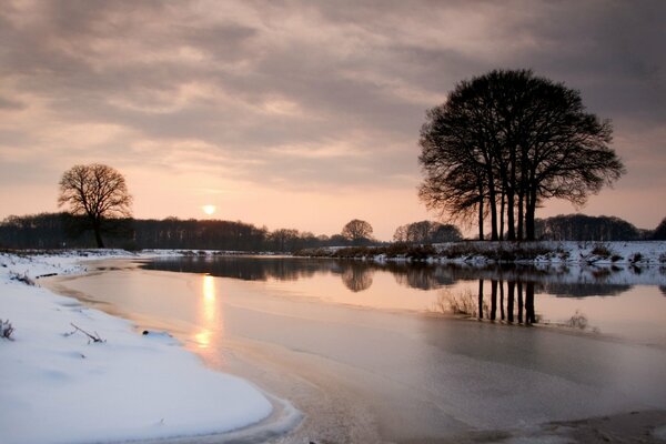 Abend Sonnenuntergang in den Bäumen am Fluss. Wintereis im Schnee 