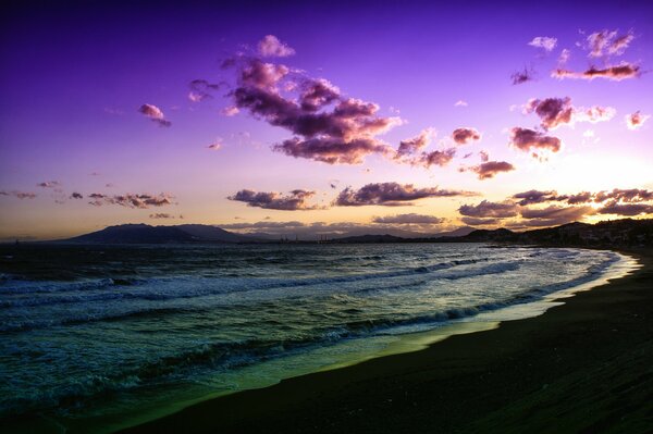 Puesta de sol lila sobre la playa dejando olas en la orilla