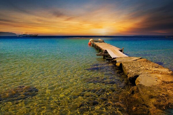 A bridge going into the sea against the background of sunset