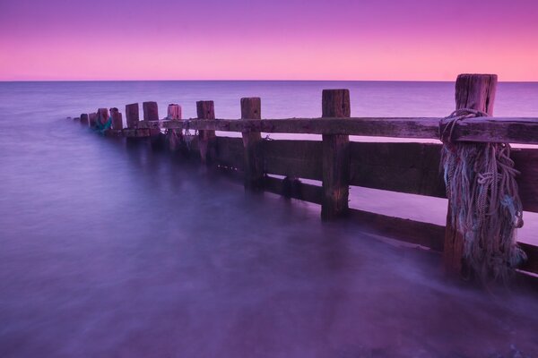 Wooden pillars in the ocean against a lilac sky