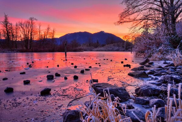 Invierno, puesta de sol en las montañas. Árboles junto al río con piedras